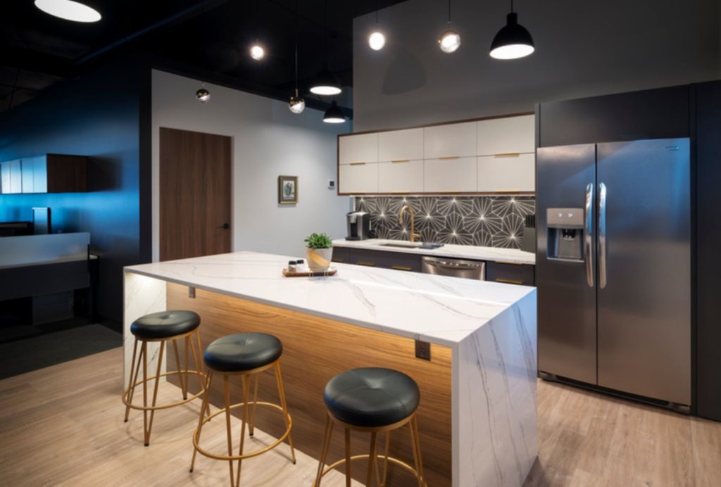 Modern designed employee kitchen area at Penticton Law firm with white cupboards, white counter top, light wood island, gold hardware and double door stainless steel fridge.