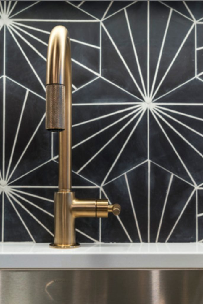 Gold kitchen faucet and black backsplash with white geometric pattern.