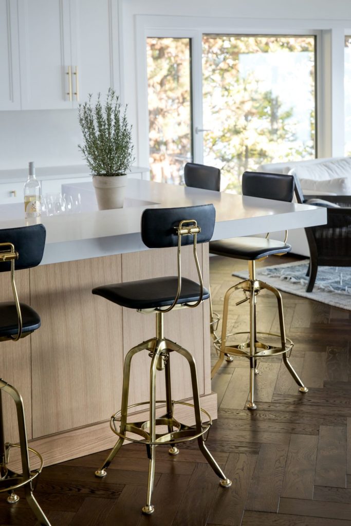 Light wood Kitchen island with white countertop, and contemporary black and gold stools.