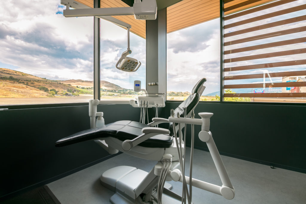 Dental exam chair in room with large windows on two walls.