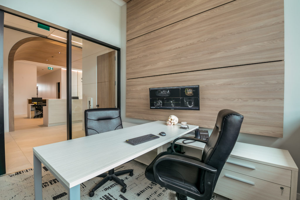 Modern office in with light wood feature wall and glass doors.