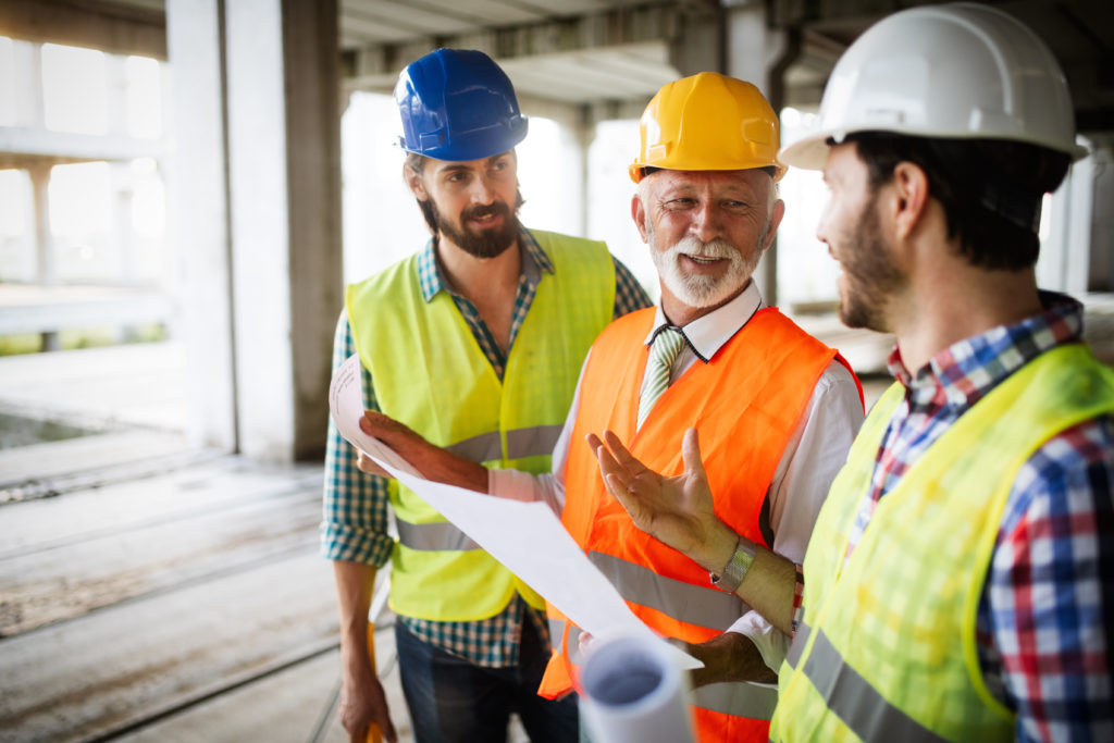 three construction workers looking at a blueprint and chatting on a building site