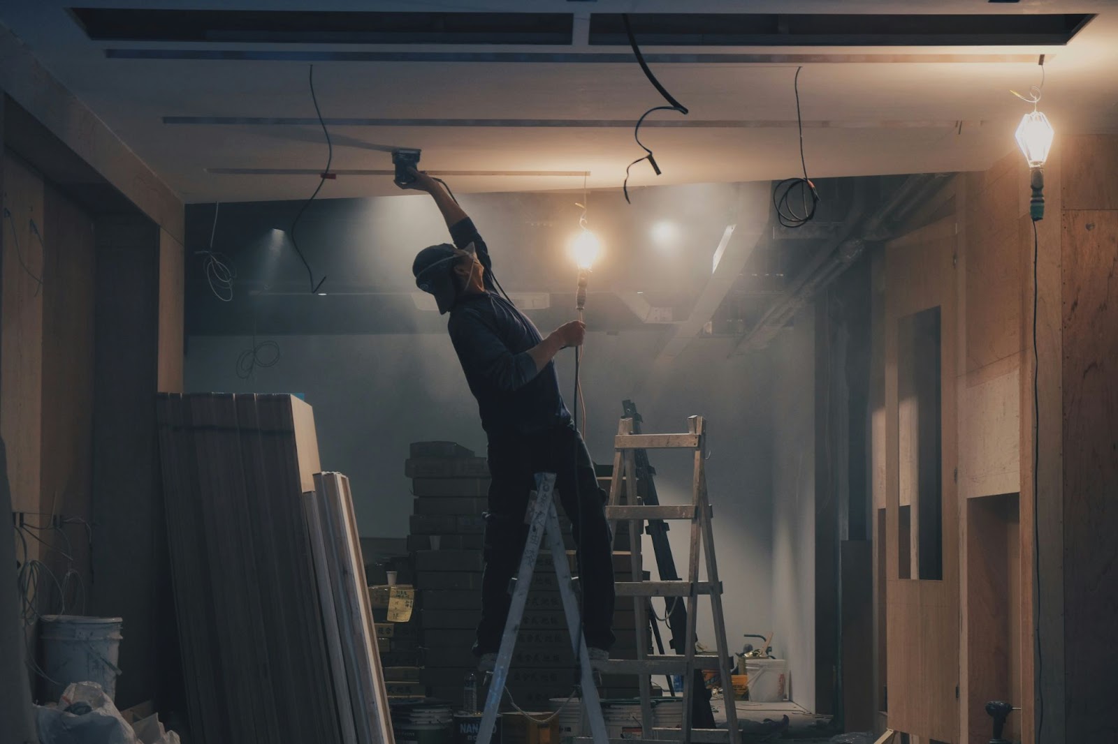 A man working on the ceiling of a construction project with bare bulbs as light.