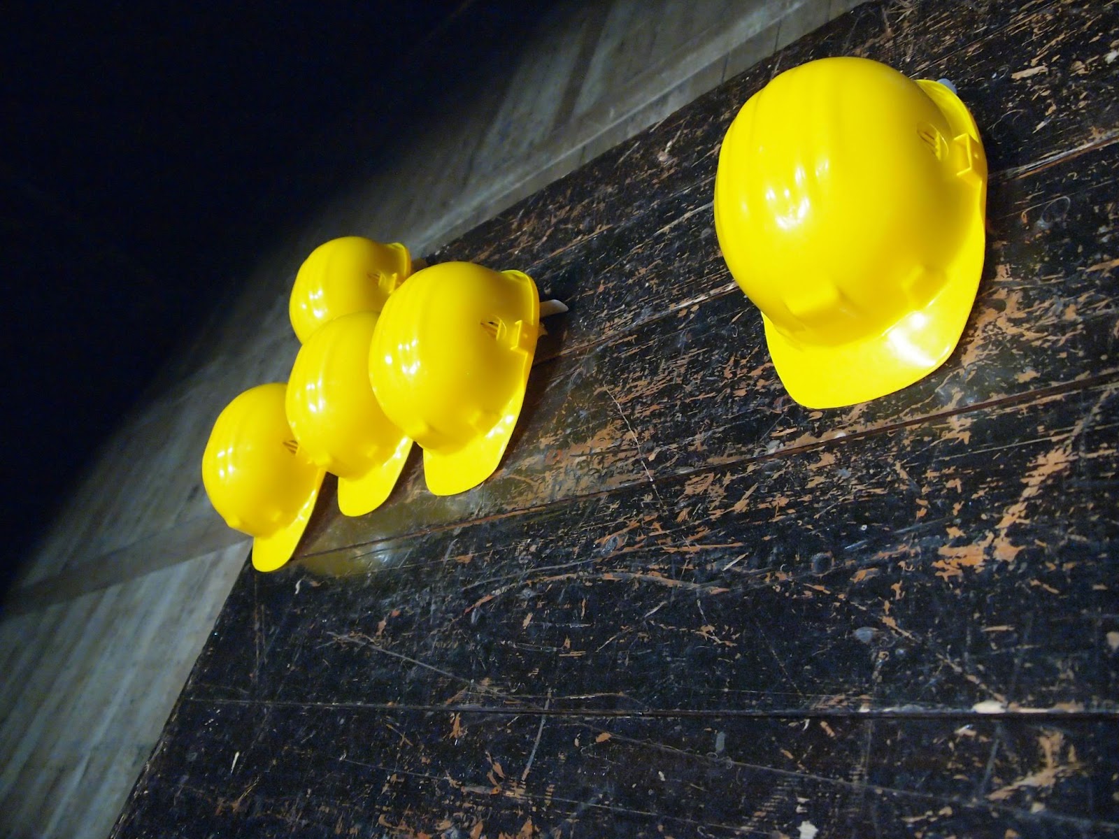 Five yellow hard hats hanging on a scratched up wooden wall. 