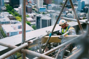 A man working in scaffolding on top of a building with cityscape in the background.