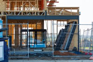 A frame of a house in a construction site with a fence around it.